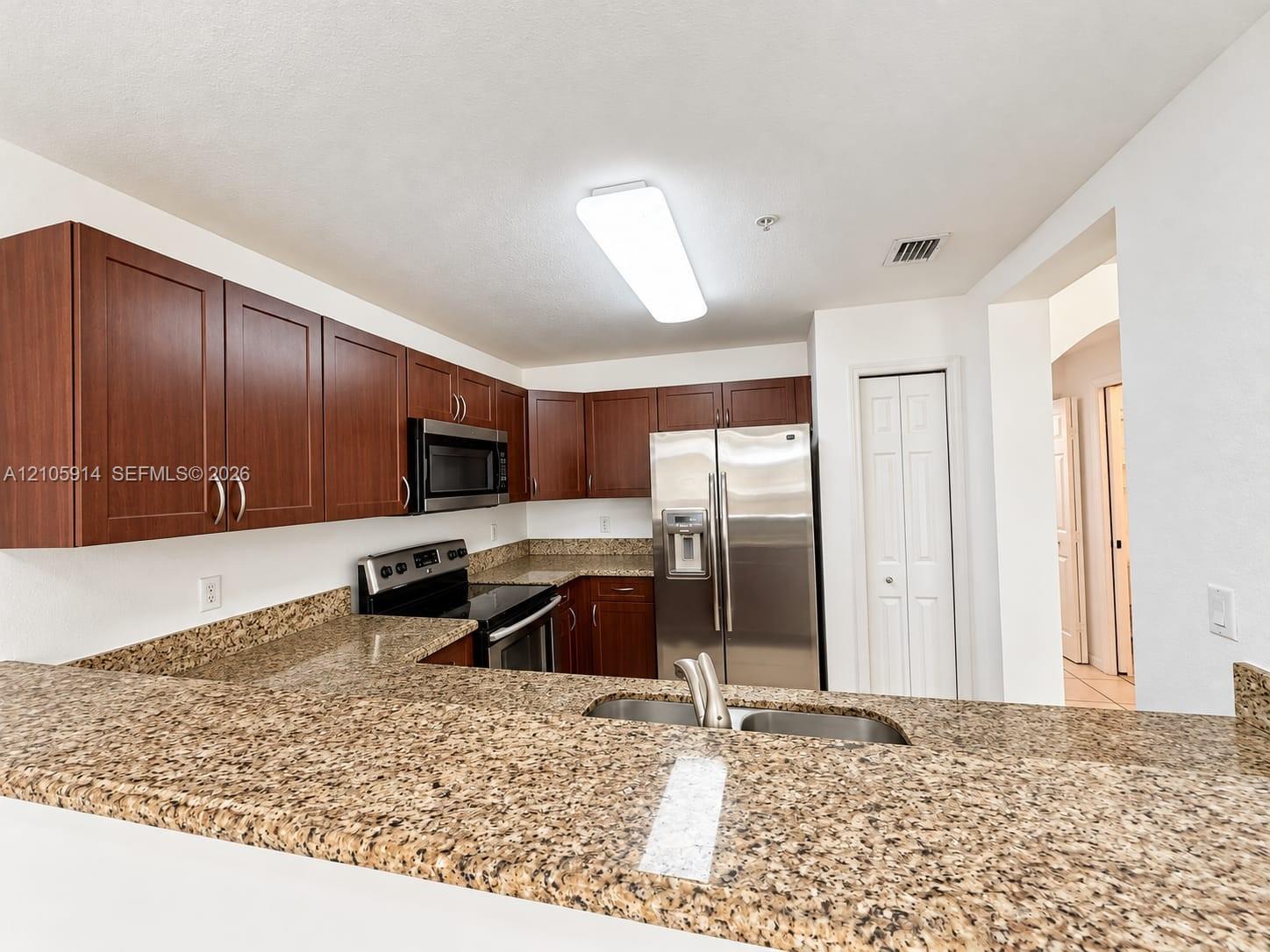 Kitchen featuring stained wood cabinetry, stone-surface countertops, stainless steel appliances, dual-basin sink, and integrated breakfast bar