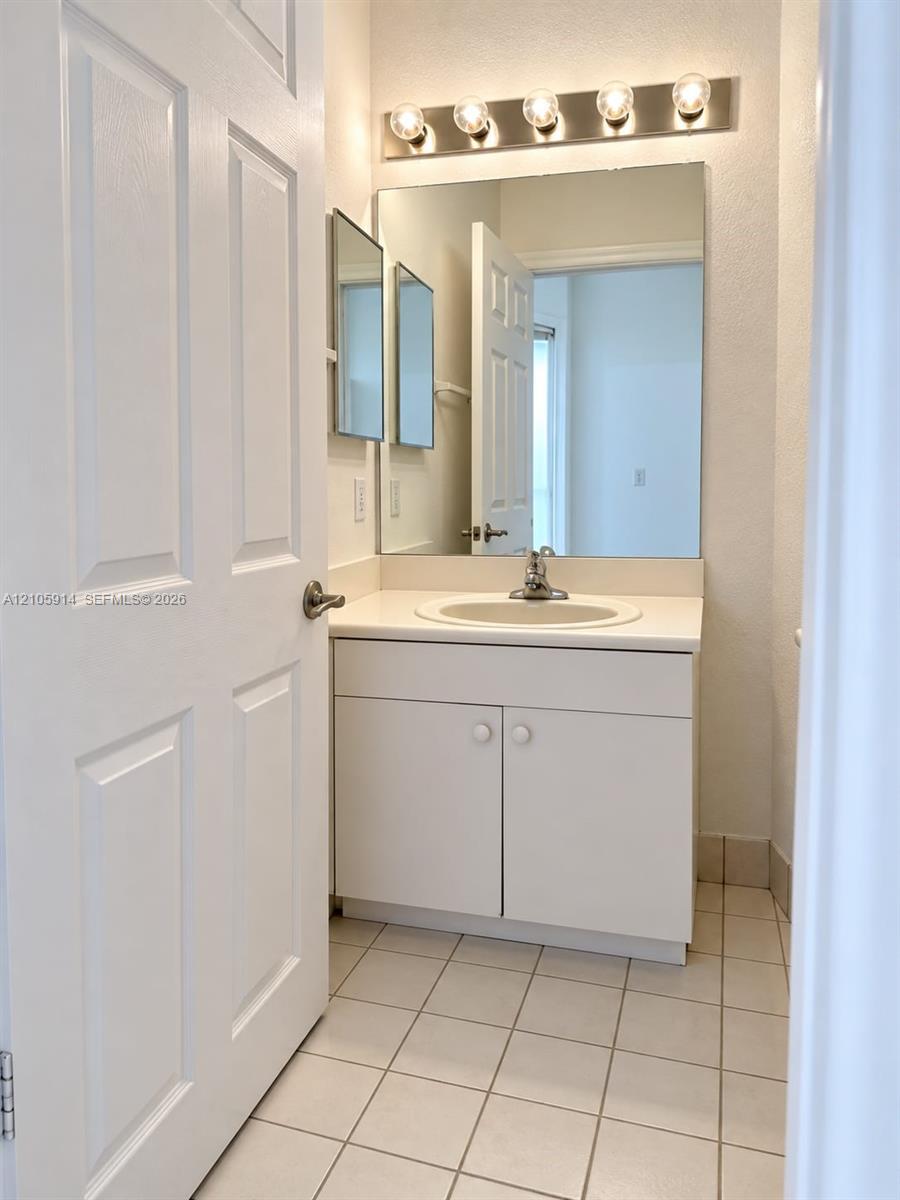 Vanity cabinet with a white countertop and integrated sink, wall-mounted mirror, five-light fixture, and ceramic tile flooring