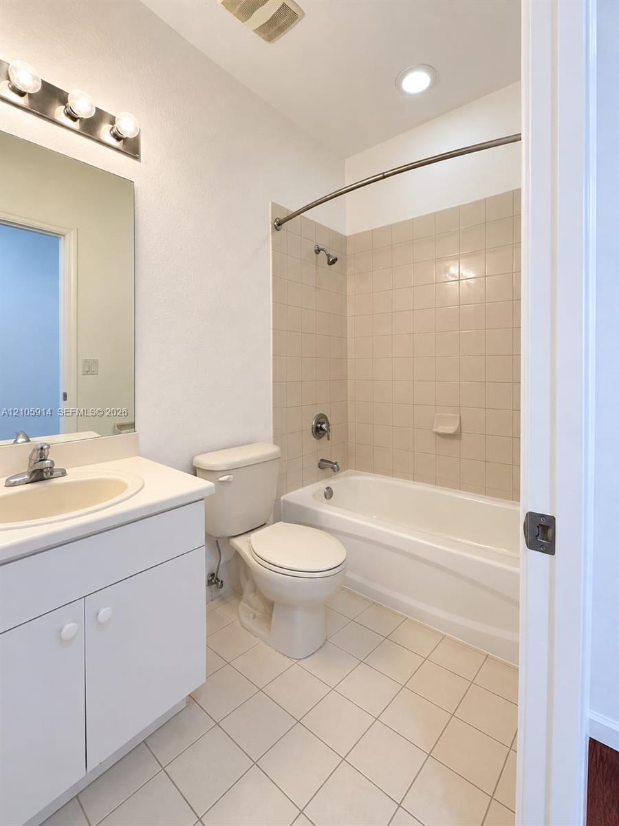 Bathroom featuring a white vanity cabinet, solid-surface countertop with an integrated sink, tiled tub surround, and a curved shower curtain rod