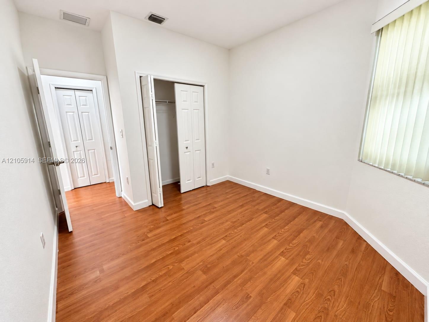 Room featuring wood-finish flooring, white walls, vertical window blinds, and dual bi-fold door closets