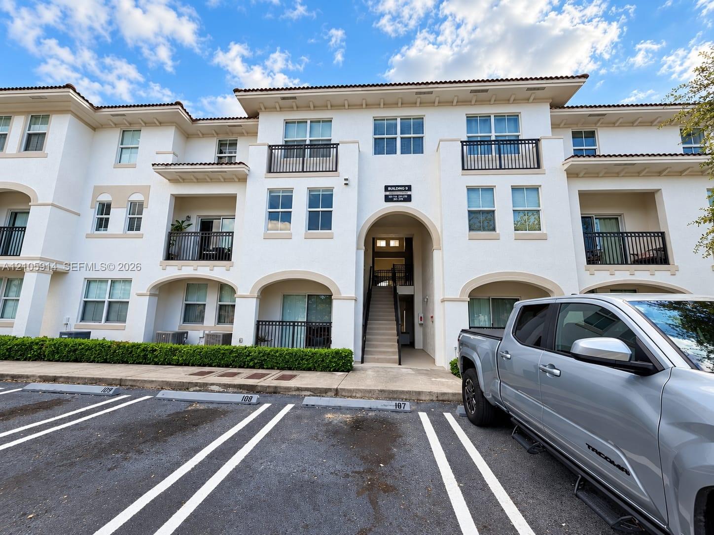 Multi-story exterior featuring a light-toned stucco facade, arched architectural detailing, and private balconies with black metal railings Multi-story exterior featuring a light-toned stucco facade, arched architectural detailing, and private balconies with black metal railings