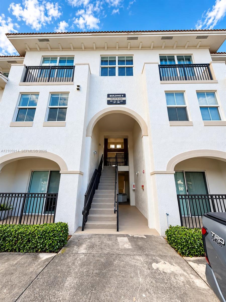 Stucco exterior featuring arched entryways, multi-level balconies with black metal railings, and a tiled roofline