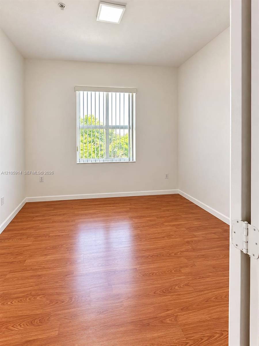 Interior space featuring wood-finish flooring, a neutral color palette, a rectangular window with vertical blinds, and a recessed ceiling light fixture