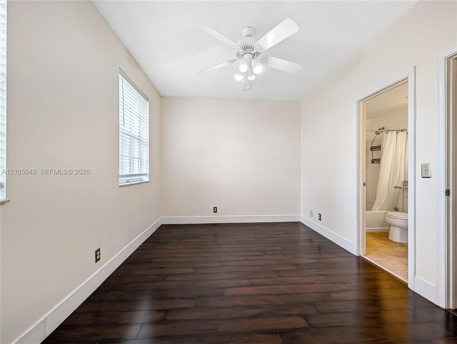Room featuring dark wood-finish flooring, neutral wall tones, a ceiling fan with integrated lighting, and horizontal window blinds