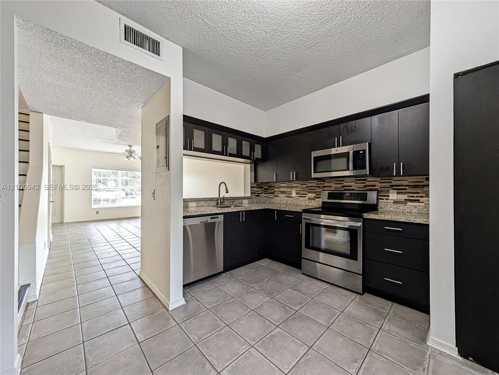 Kitchen featuring dark cabinetry, stone-finish countertops, stainless steel appliances, a multi-tone tile backsplash, and ceramic floor tiling