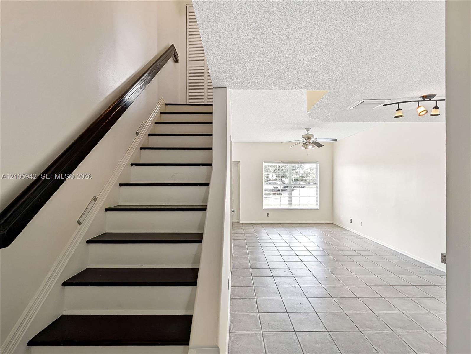 Staircase featuring dark wood-finish treads and a high-contrast railing, complemented by ceramic tile flooring, a ceiling fan, and multi-light track lighting