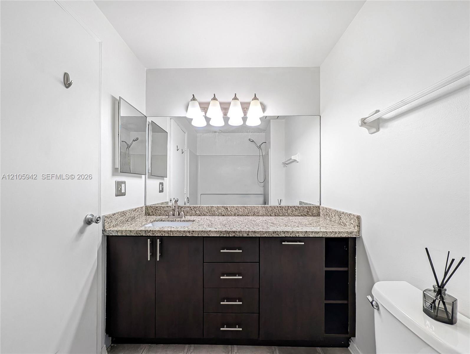 Bathroom vanity featuring dark-toned cabinetry with integrated shelving, stone-finish countertop, undermount sink, and four-light fixture