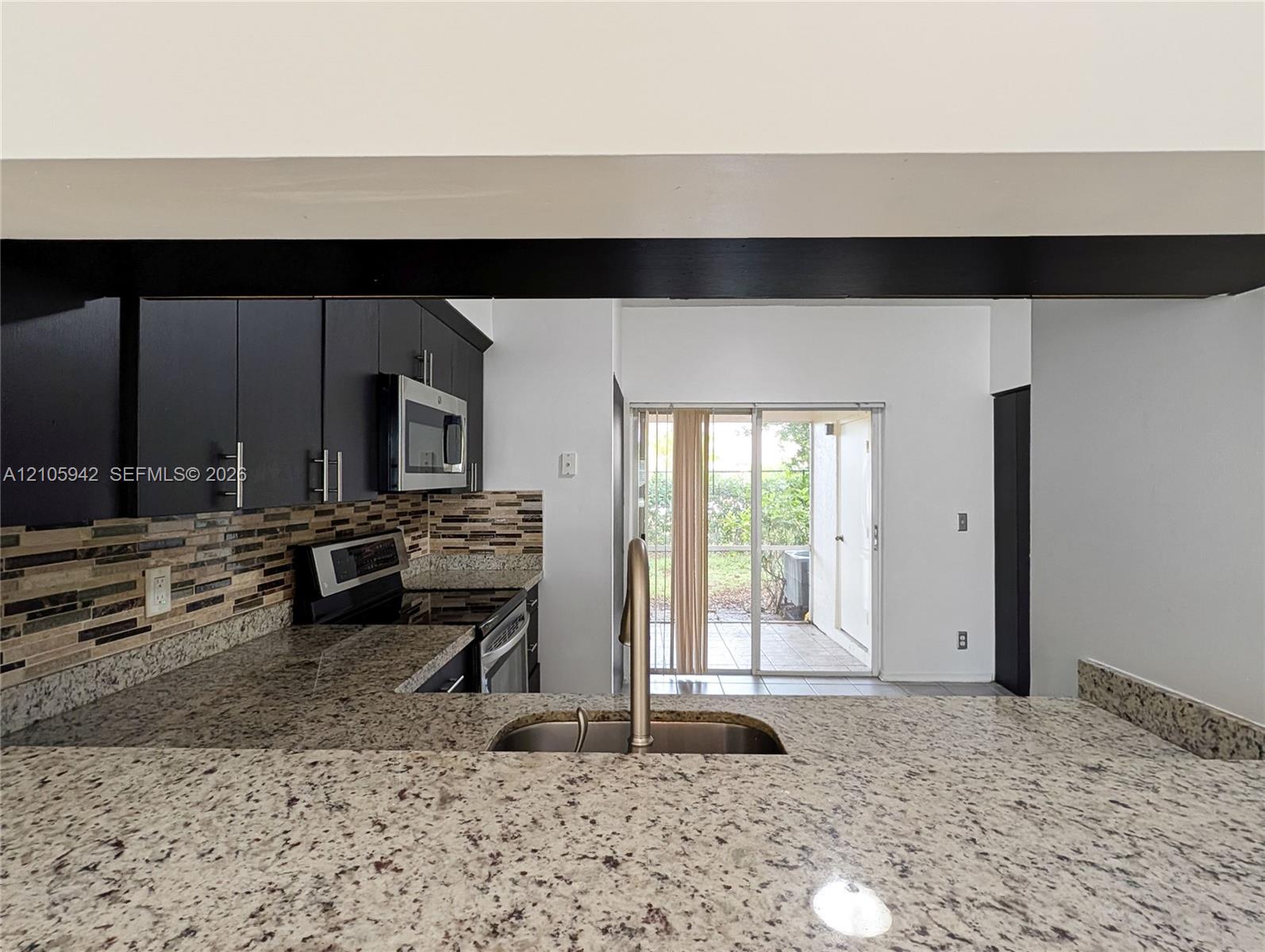 Kitchen featuring a stone-surface breakfast bar, mosaic tile backsplash, dark cabinetry, stainless steel microwave, and sliding glass doors