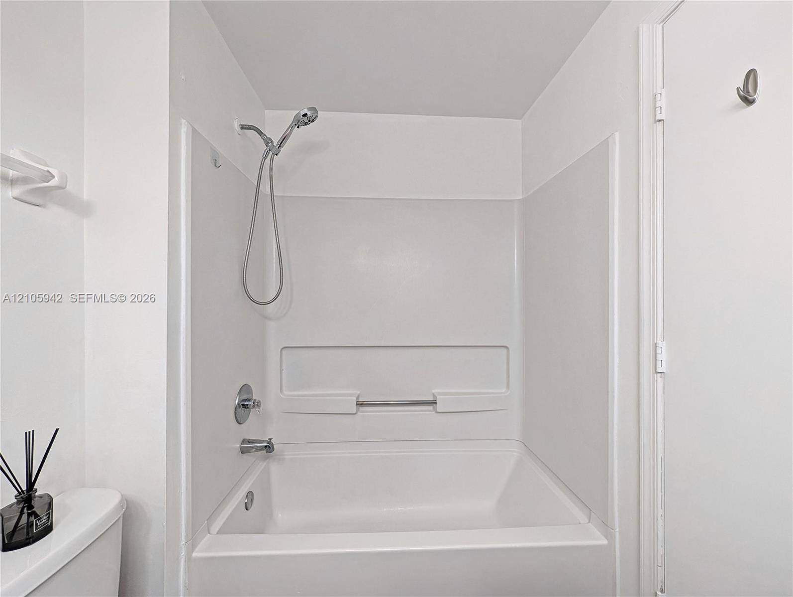 Tub-shower combination featuring a white surround, integrated shelving, and a chrome handheld shower head