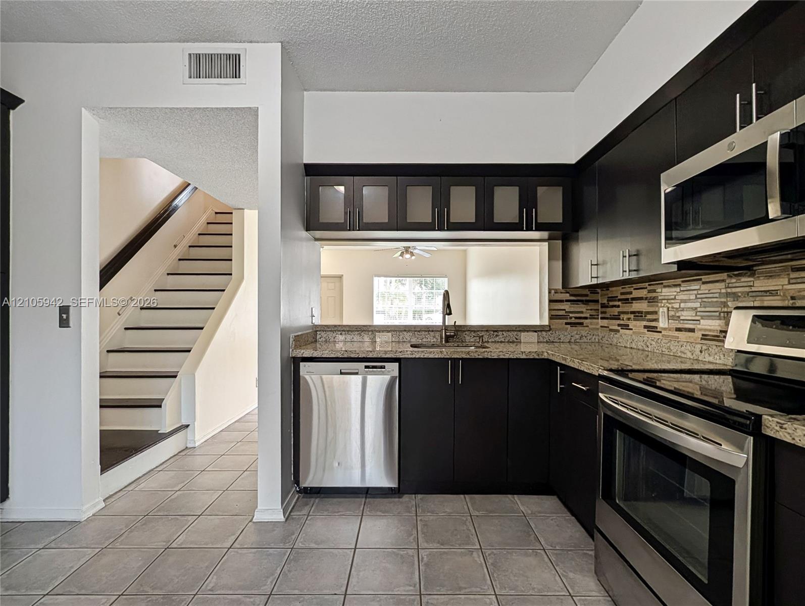 Kitchen featuring dark cabinetry, stone-finish countertops, stainless steel appliances, a glass-tile backsplash, and tiled flooring
