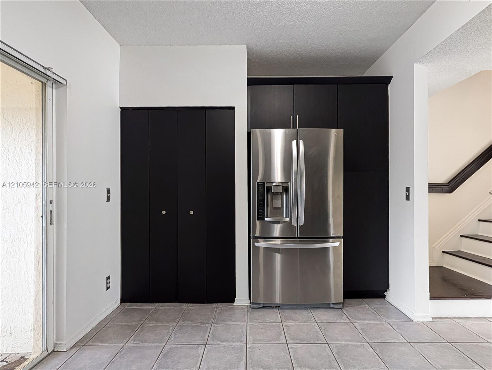Dark-toned built-in cabinetry, stainless steel French-door refrigerator, tile flooring, and sliding glass door