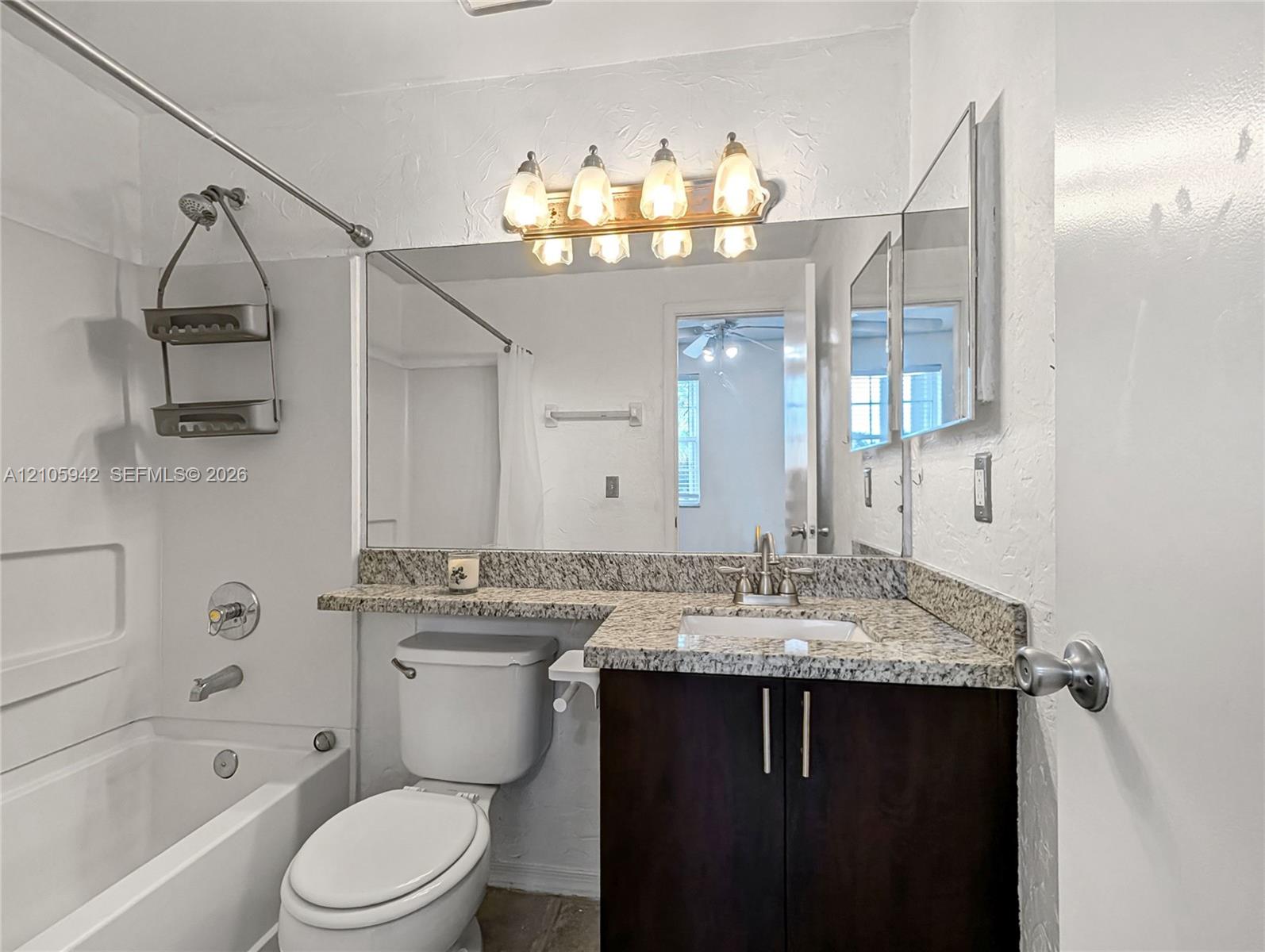 Bathroom featuring a dark-finish vanity with stone-patterned countertop, integrated basin, large wall-mounted mirror, and multi-bulb vanity lighting