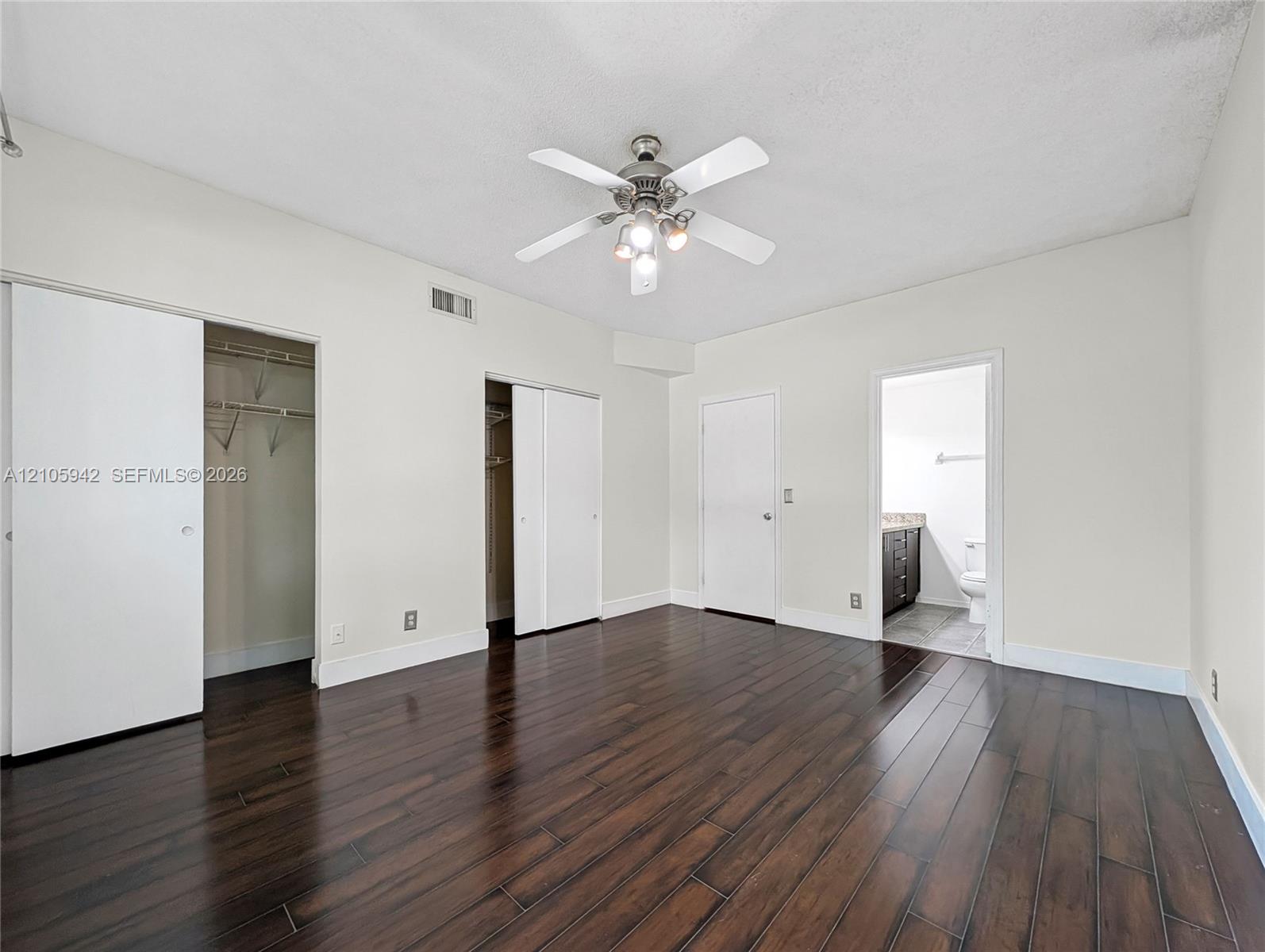 Room featuring dark wood-finish flooring, a multi-blade ceiling fan with integrated lighting, and dual reach-in closets with sliding doors