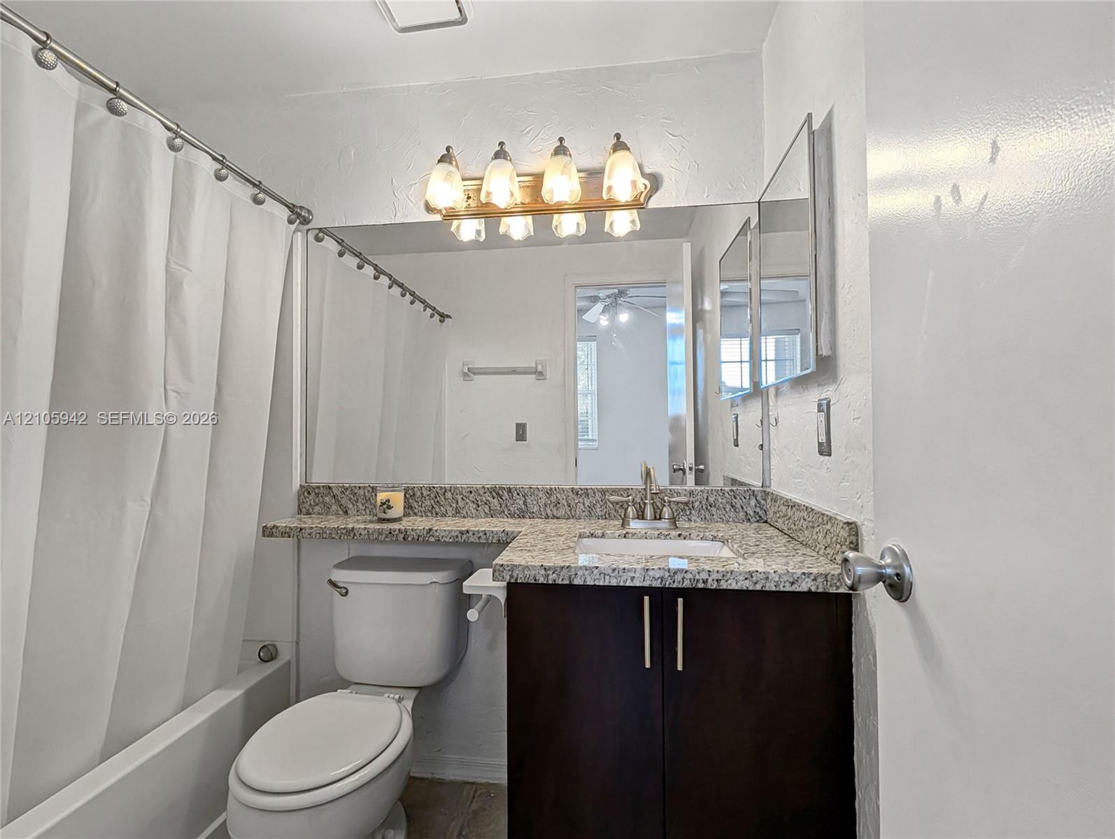 Bathroom featuring a vanity with stone-finish countertop, undermount sink, multi-light fixture, and large wall-mounted mirror