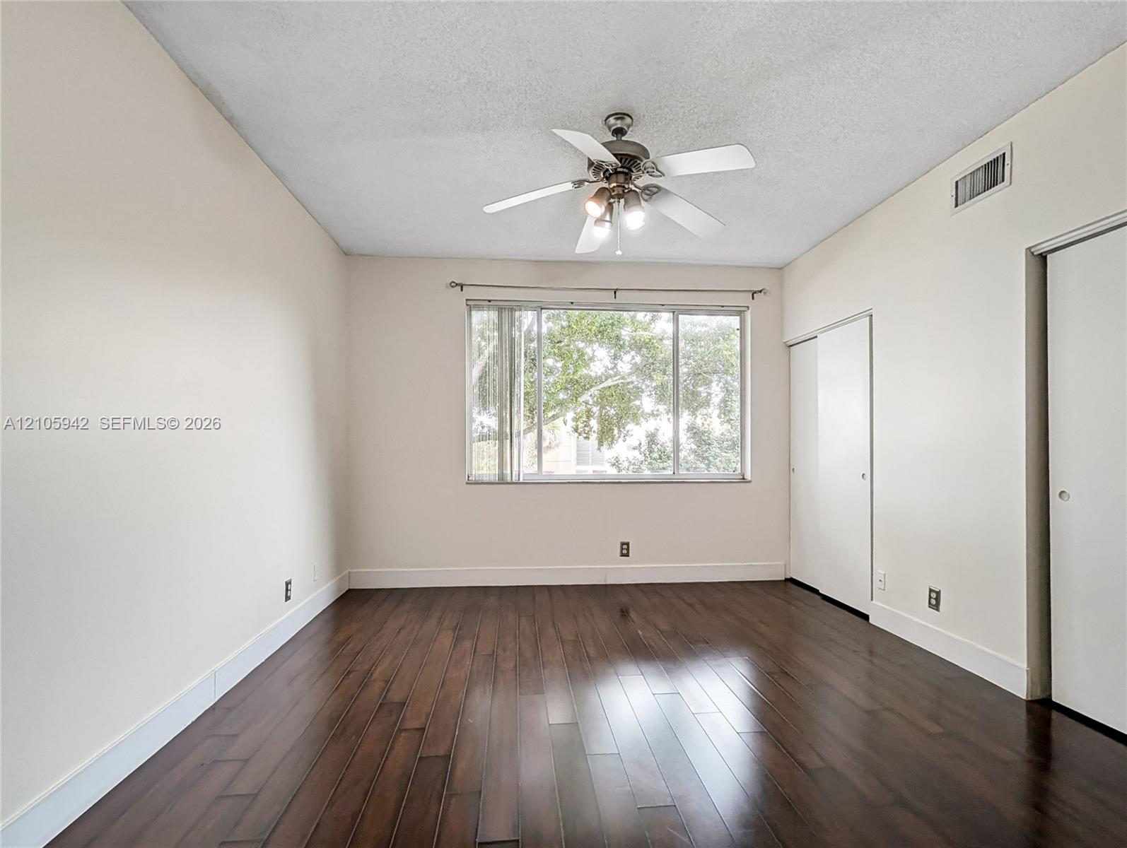 Room featuring wood-finish flooring, a ceiling fan with integrated light fixture, and a sliding-door closet