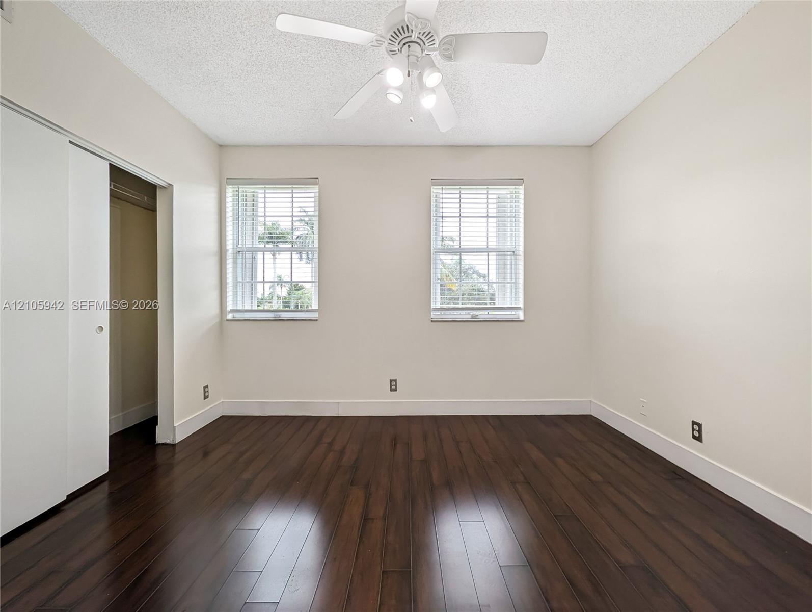Wood-finish flooring, dual windows with horizontal blinds, white sliding closet doors, and ceiling fan with integrated lighting