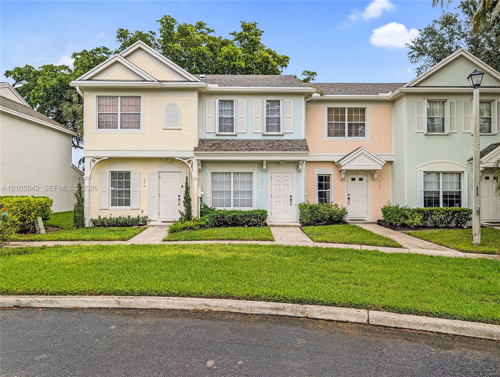 Multi-unit residential exterior featuring a multi-toned stucco facade, gabled rooflines, decorative brackets, and landscaped lawn