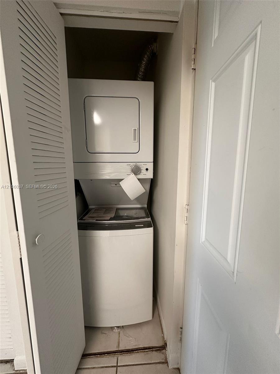 Laundry closet featuring a white stacked washer and dryer unit, louvered closet doors, and tile flooring
