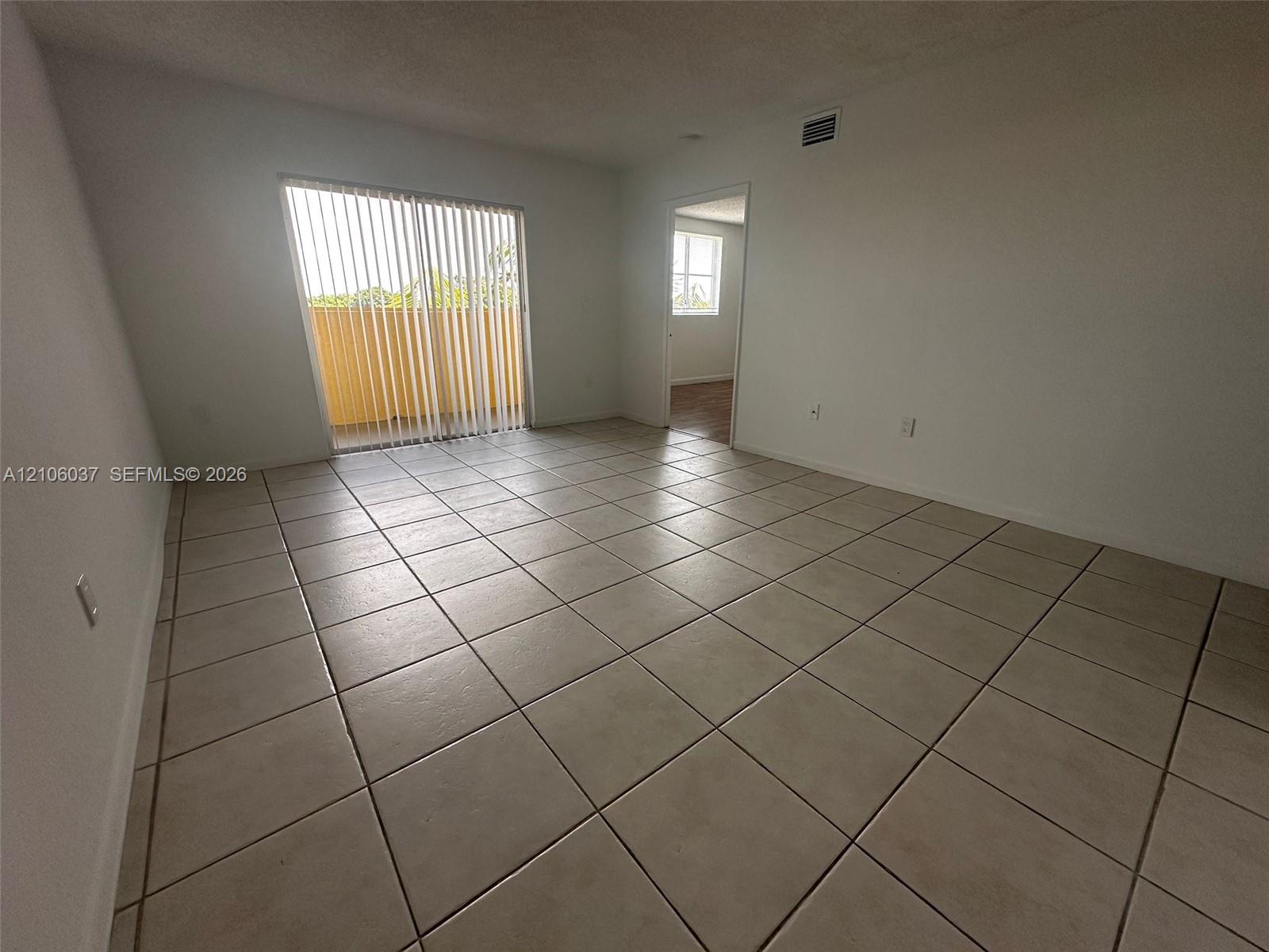 Interior room featuring large-format ceramic floor tile, sliding glass door with vertical blinds, and neutral wall tones