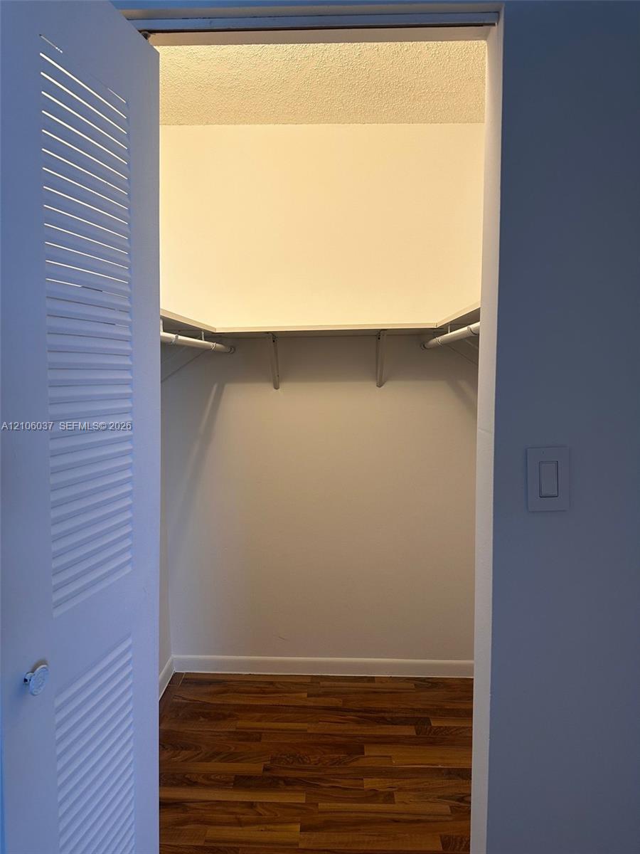 Storage space featuring louvered bi-fold doors, white shelving, a rod for hanging items, and wood-finish flooring