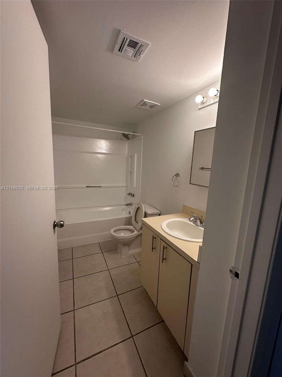 Bathroom featuring ceramic tile flooring, a single-sink vanity with a solid-surface countertop, and a tub-shower combination with a surround