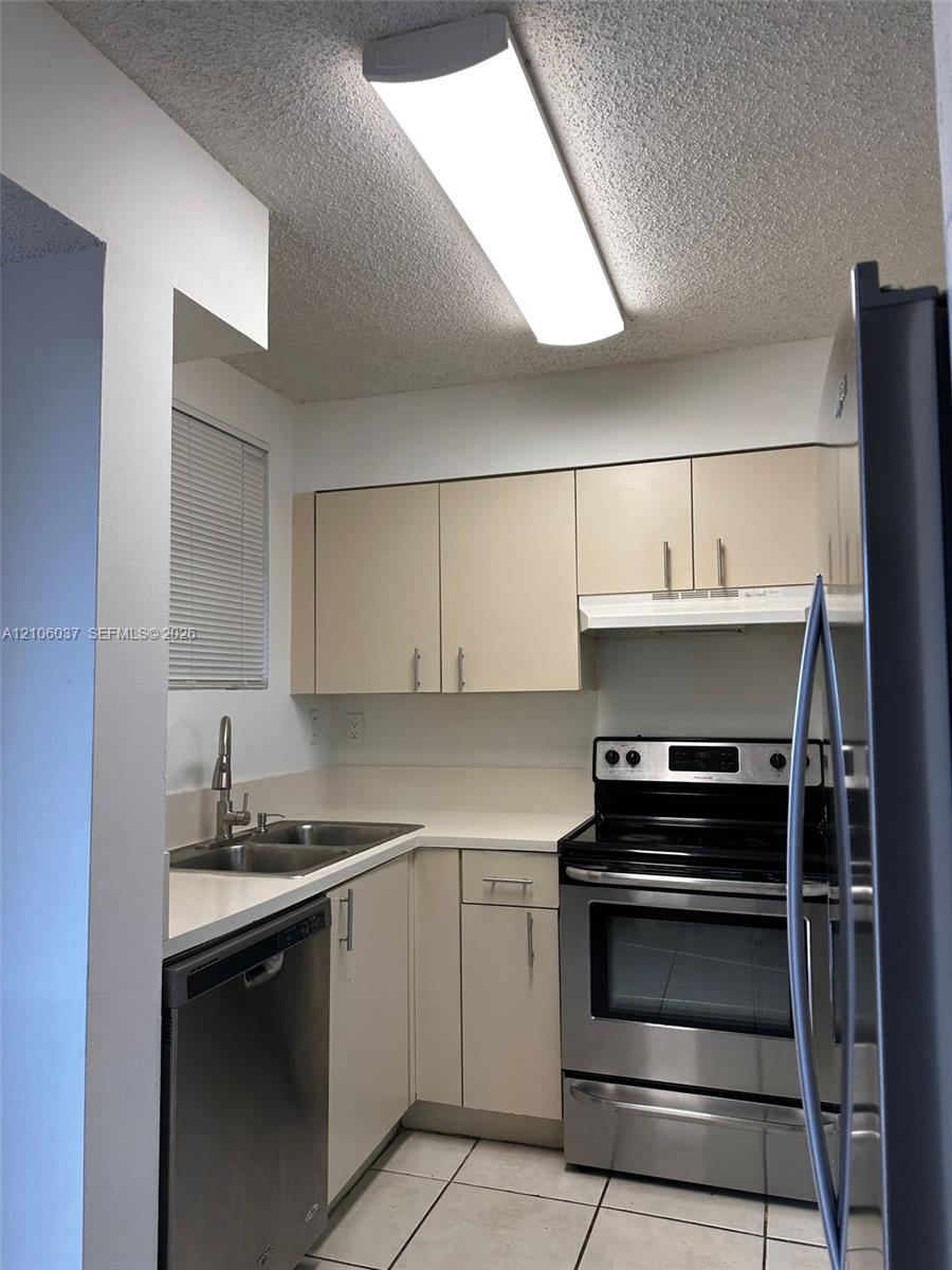 Kitchen featuring stainless steel appliances, double-basin sink with high-arc faucet, solid-surface countertops, flat-panel cabinetry, and tile flooring