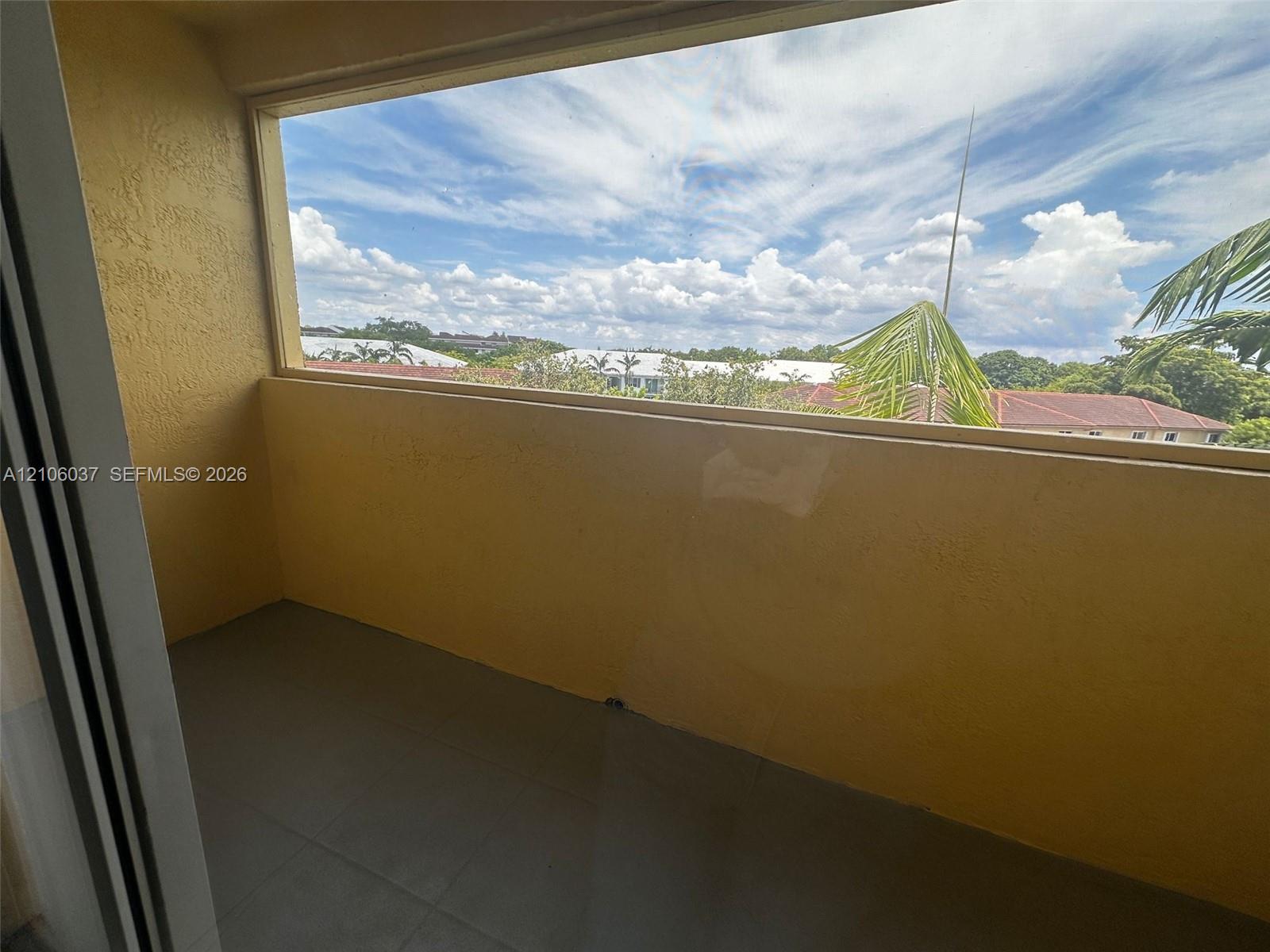 Covered balcony featuring concrete flooring, textured walls, and a large window enclosure