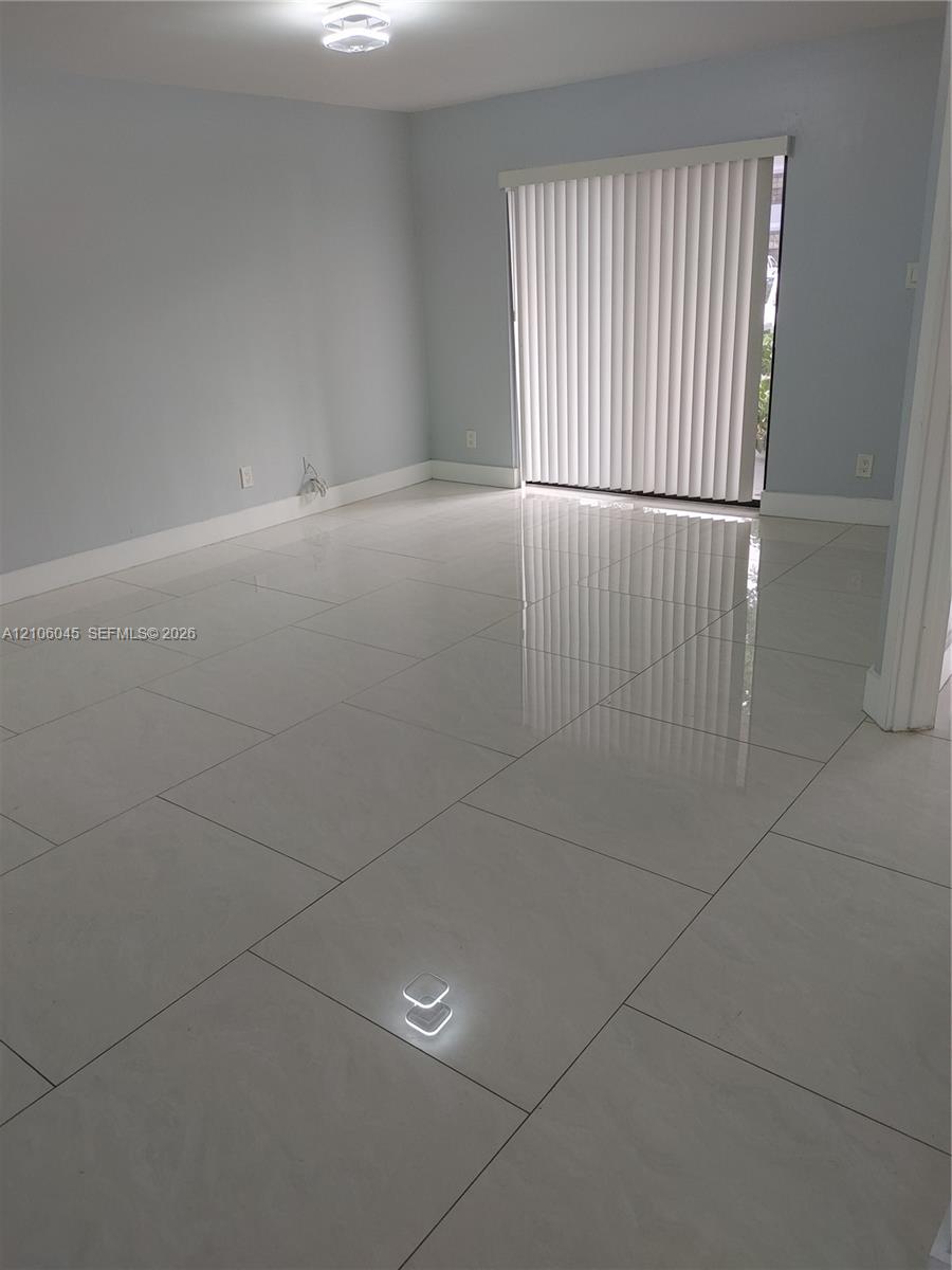 Neutral-toned interior featuring large-format polished tile flooring, light-reflective surfaces, a sliding glass door, and a flush-mount ceiling light fixture