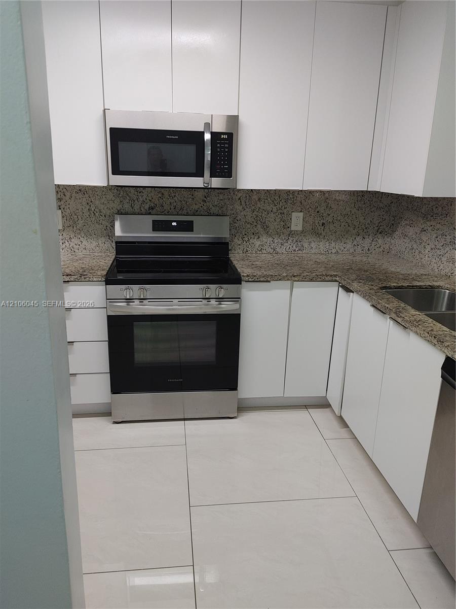 Kitchen featuring white flat-panel cabinetry, stone countertops, stainless steel appliances, and large-format tile flooring