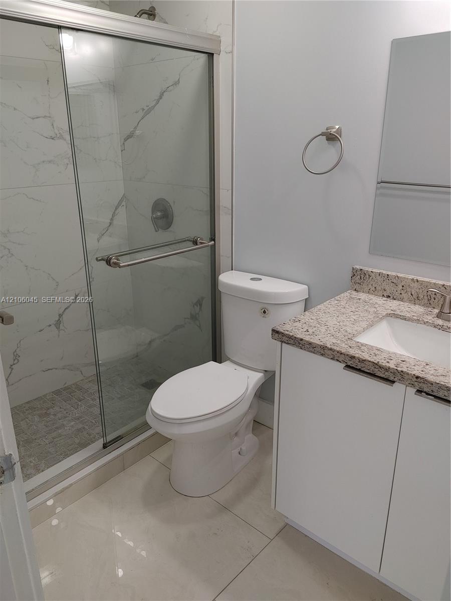 Walk-in shower with floor-to-ceiling large-format tile surround, frameless glass door, vanity with speckled stone-finish countertop, and polished chrome fixtures