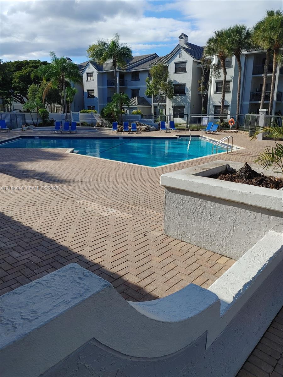 In-ground pool surrounded by a herringbone-pattern brick paver deck, stucco-finished retaining walls, and mature palm trees