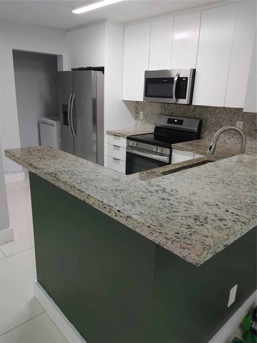 Kitchen featuring stone countertops, white shaker-style cabinetry, stainless steel appliances, and a breakfast bar