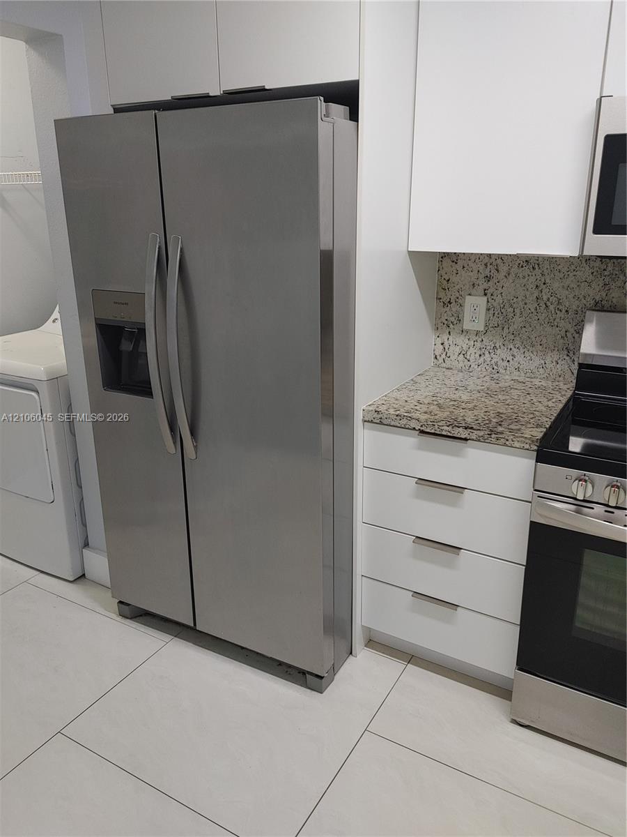 Stainless steel side-by-side refrigerator, white flat-panel cabinetry, stone-surface countertops, and large-format tile flooring