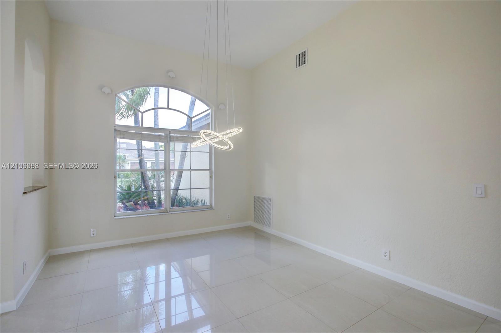 High-ceilinged room featuring large arched window, polished tile flooring, and contemporary multi-ring pendant lighting
