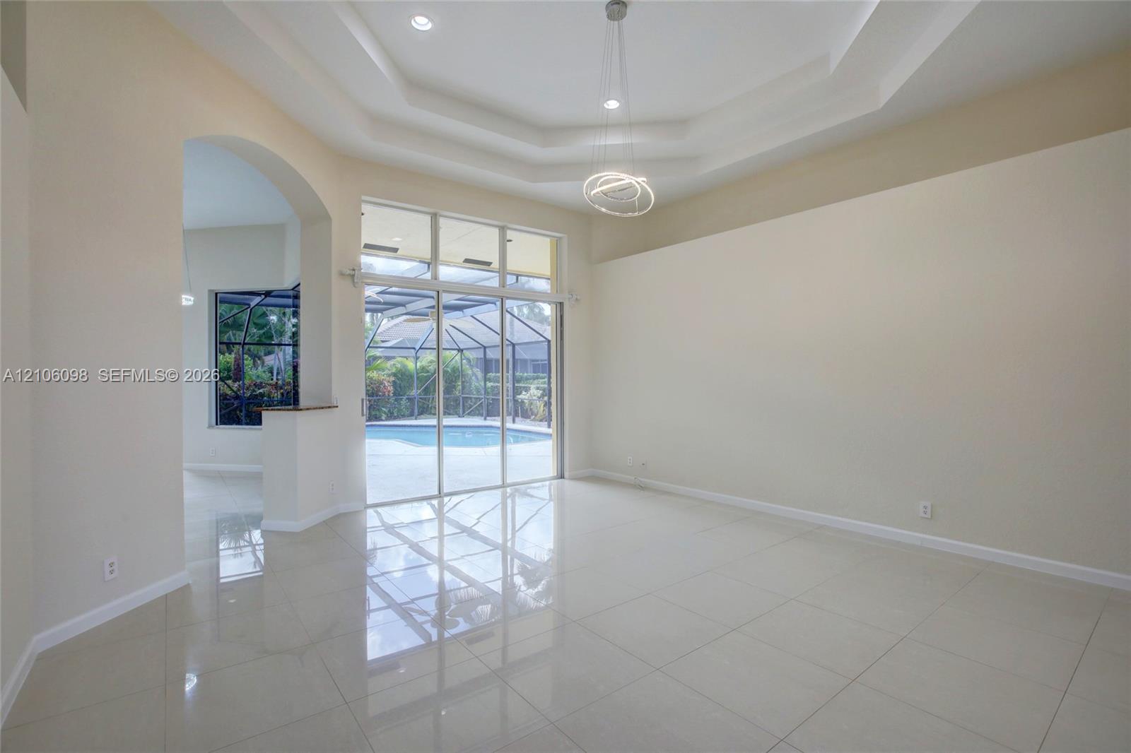 Interior space featuring tile flooring, a recessed tray ceiling, architectural archway, and expansive sliding glass doors opening to a screened pool enclosure