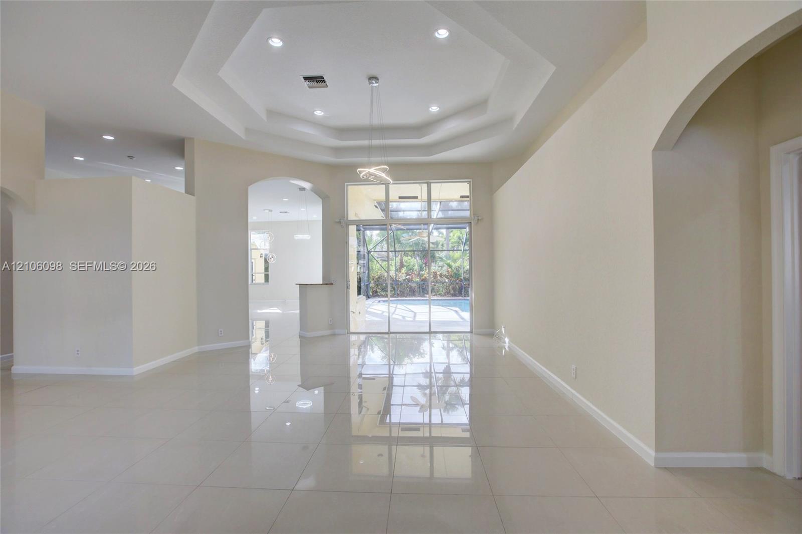 Open interior featuring polished tile flooring, tray ceilings with recessed lighting, an architectural archway, and expansive floor-to-ceiling glass panel doors