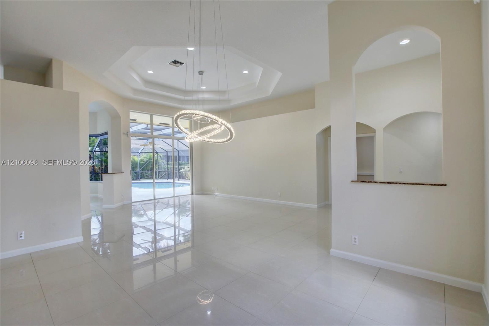 Octagonal tray ceiling, polished tile flooring, contemporary circular chandelier, arched wall cutouts, and expansive sliding glass doors