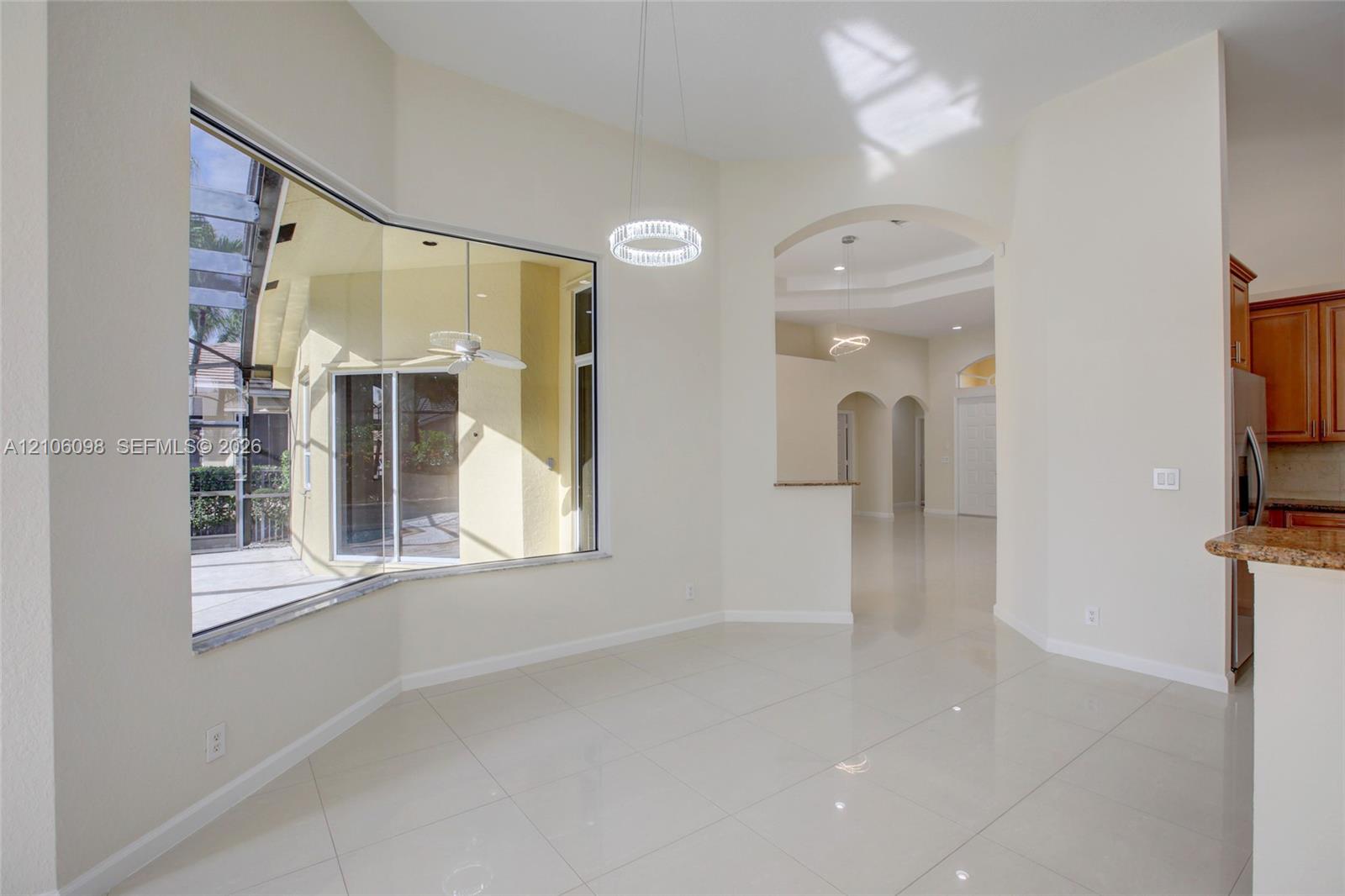 Large bay window, polished tile flooring, arched architectural openings, circular LED pendant lighting, and stone-surfaced breakfast bar