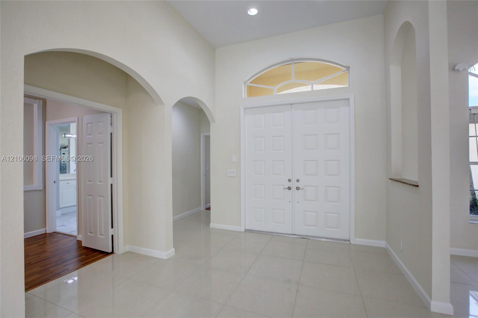 Double front doors with an arched transom window, high ceilings, tile flooring, and decorative arched wall niches