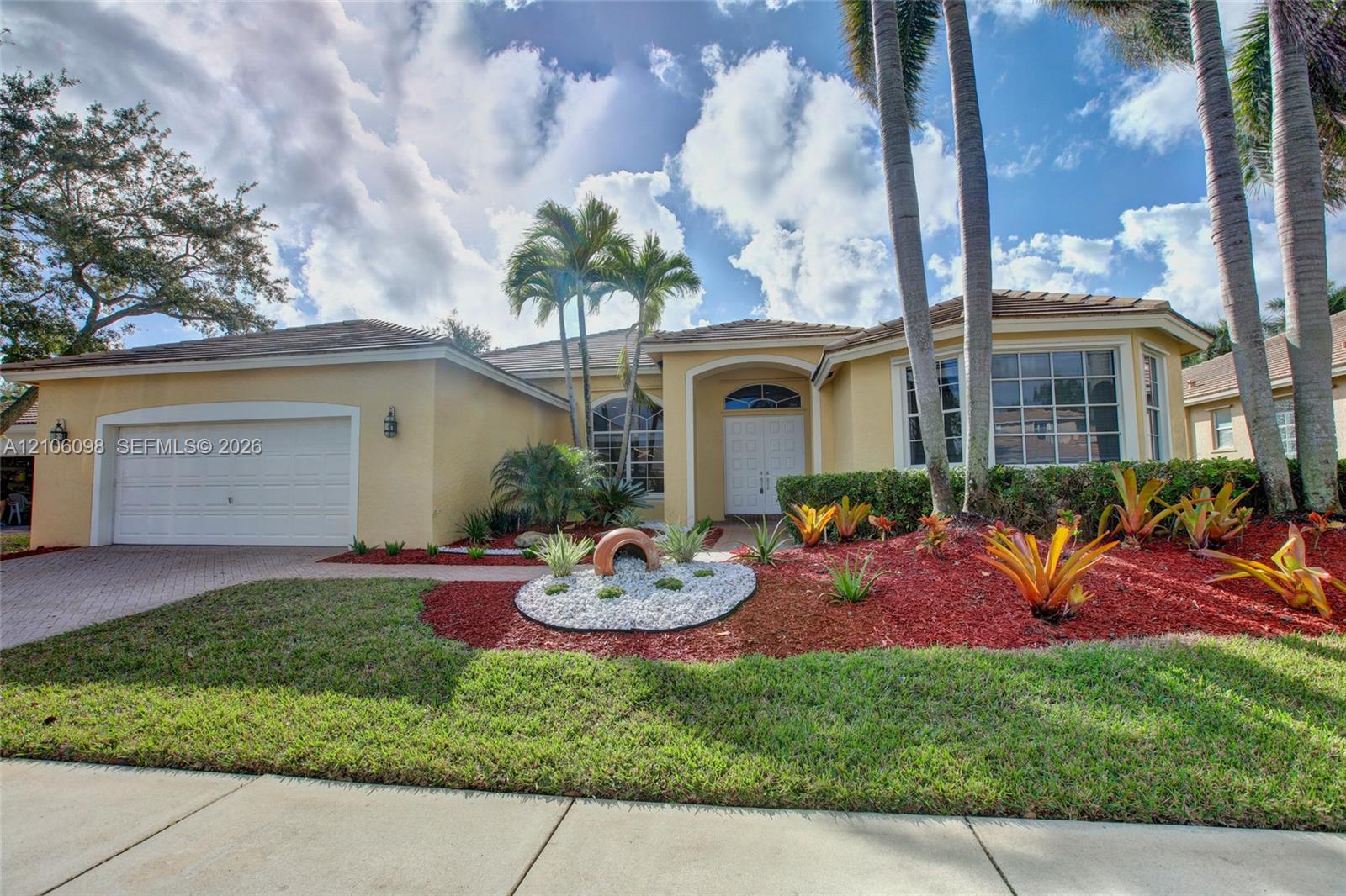 Single-story residence featuring a stucco exterior, multi-pane windows, a paver driveway, an attached two-car garage, and established tropical landscaping