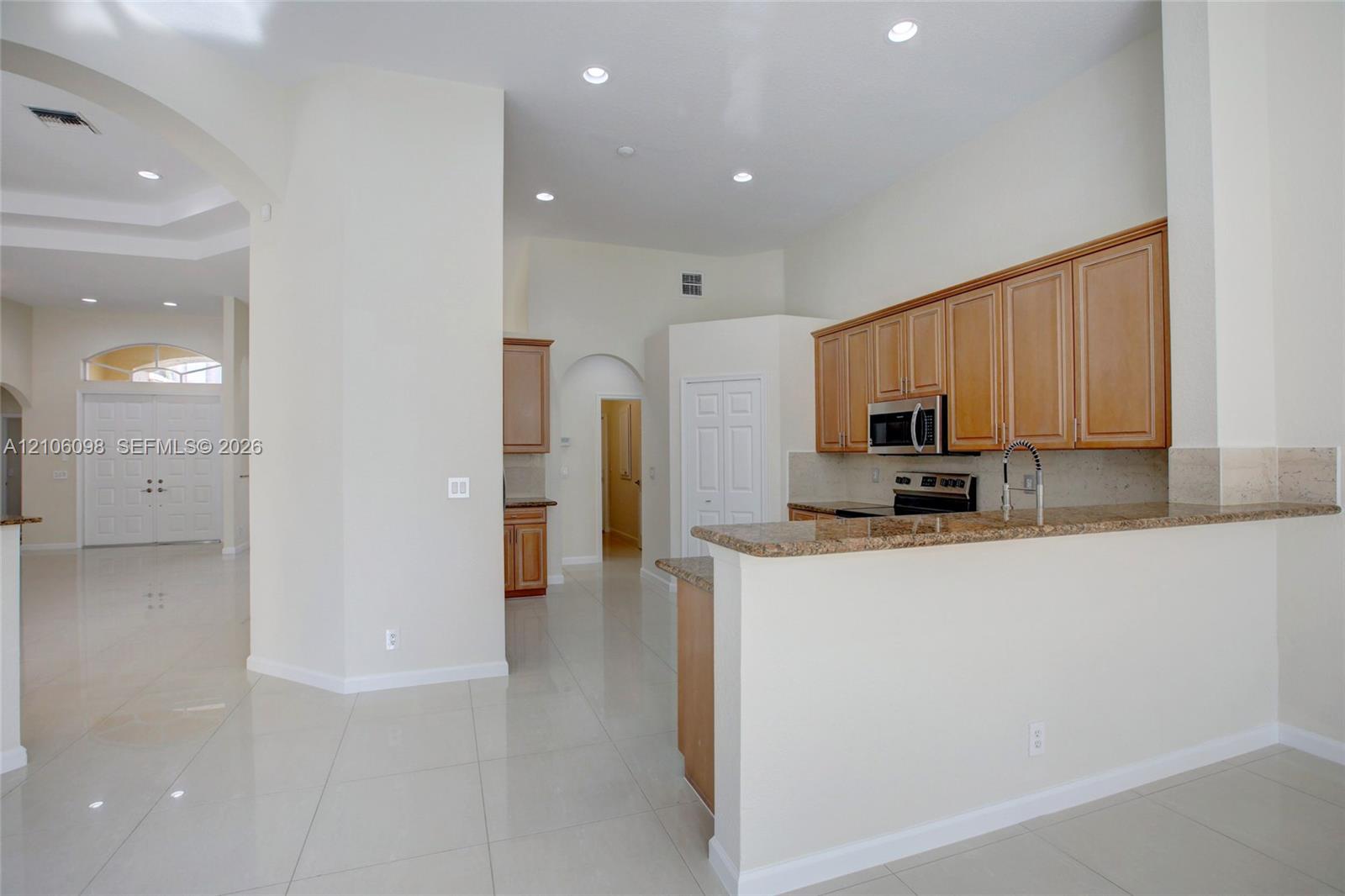 Kitchen featuring stone countertops, natural wood-finish cabinetry, built-in stainless steel appliances, recessed ceiling lighting, and tile flooring throughout