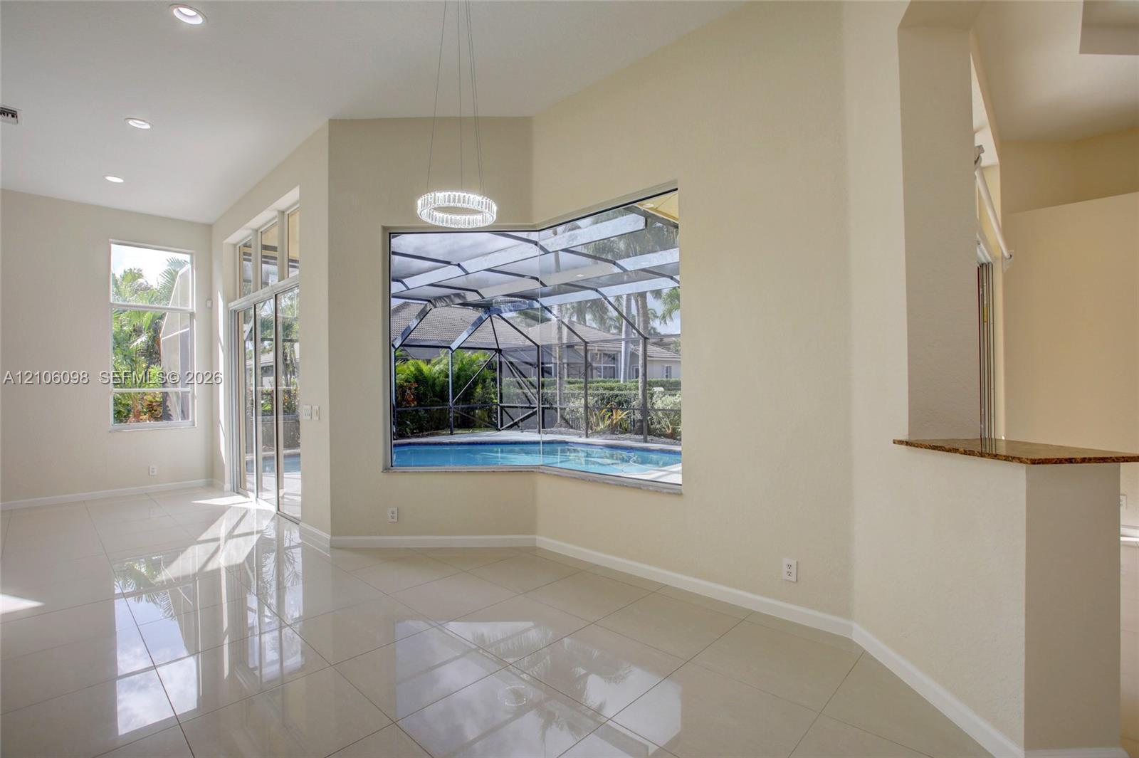 Open-concept interior featuring polished tile flooring, recessed lighting, a built-in stone-surface counter, and large windows encompassing a screened-in pool enclosure