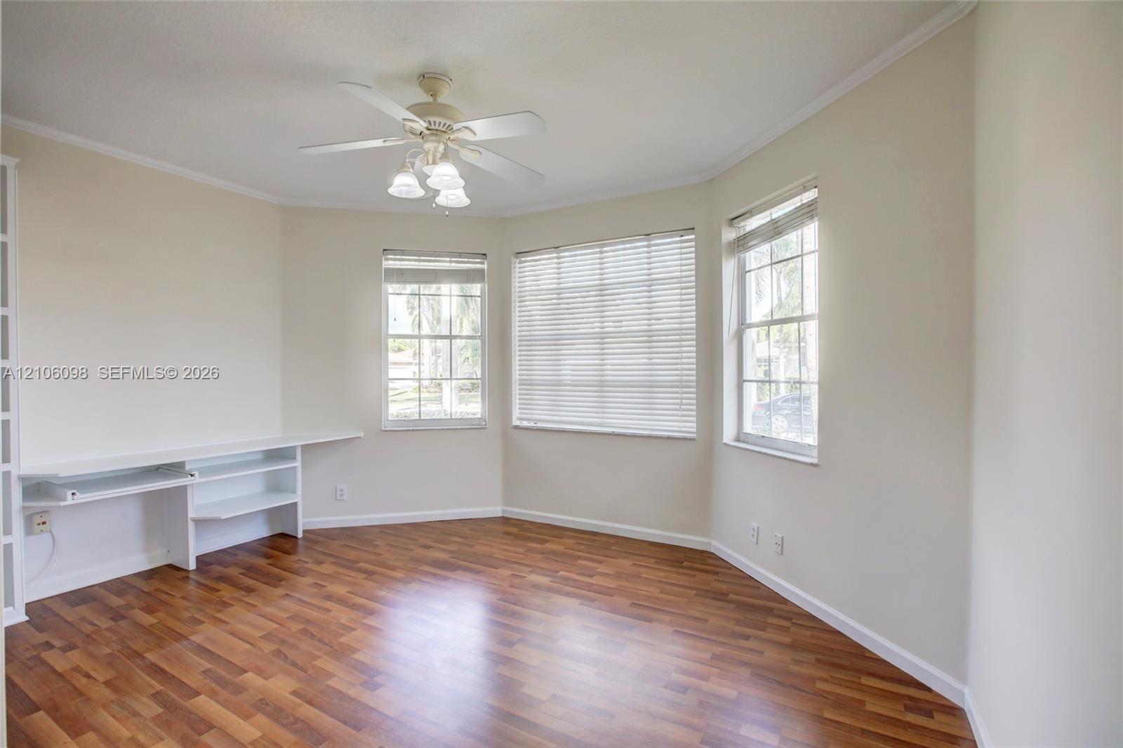 Room featuring wood-finish flooring, built-in shelving, a ceiling fan with integrated lighting, and multiple windows with horizontal blinds