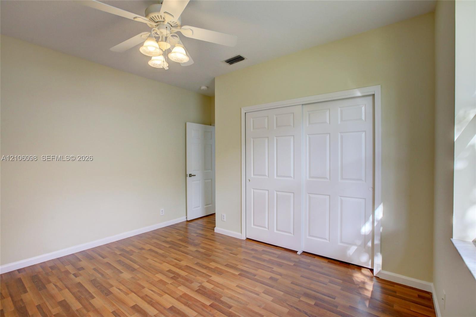 Wood-finish flooring, white paneled closet doors, six-panel interior door, and multi-light ceiling fan