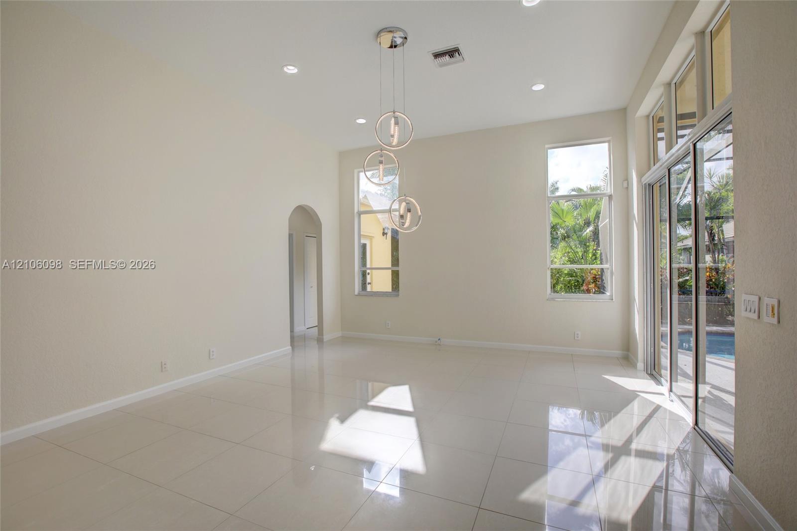 High-ceiling living area featuring large-format tile flooring, a multi-tier contemporary pendant light fixture, arched entryways, and sliding glass doors