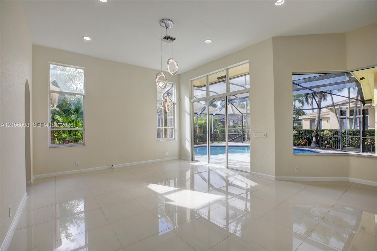 High ceilings with recessed lighting, large-format tile flooring, multi-light pendant fixture, floor-to-ceiling windows, and sliding glass doors opening to a screened-in pool enclosure