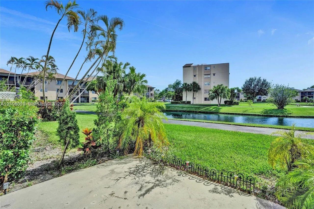 Concrete patio featuring low-profile decorative metal fencing, manicured lawn, established palm trees, and a waterway