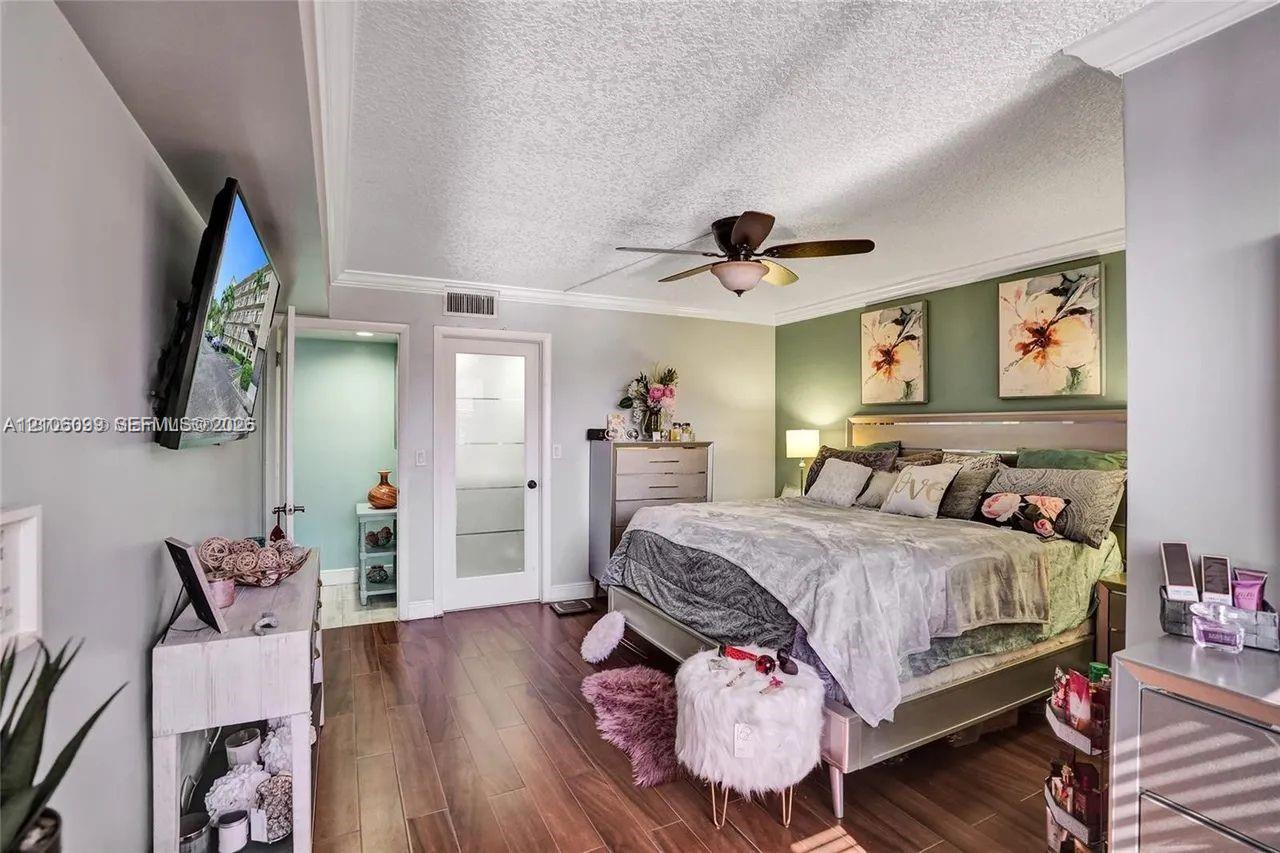 Wood-finish flooring, ceiling fan with integrated light fixture, accent wall, and glass-paneled interior door