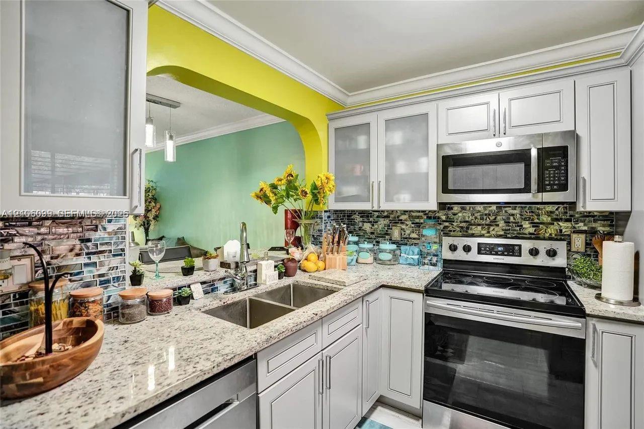 Kitchen featuring shaker-style cabinetry with frosted glass inserts, speckled stone countertops, mosaic tile backsplash, and stainless steel appliances including a built-in microwave