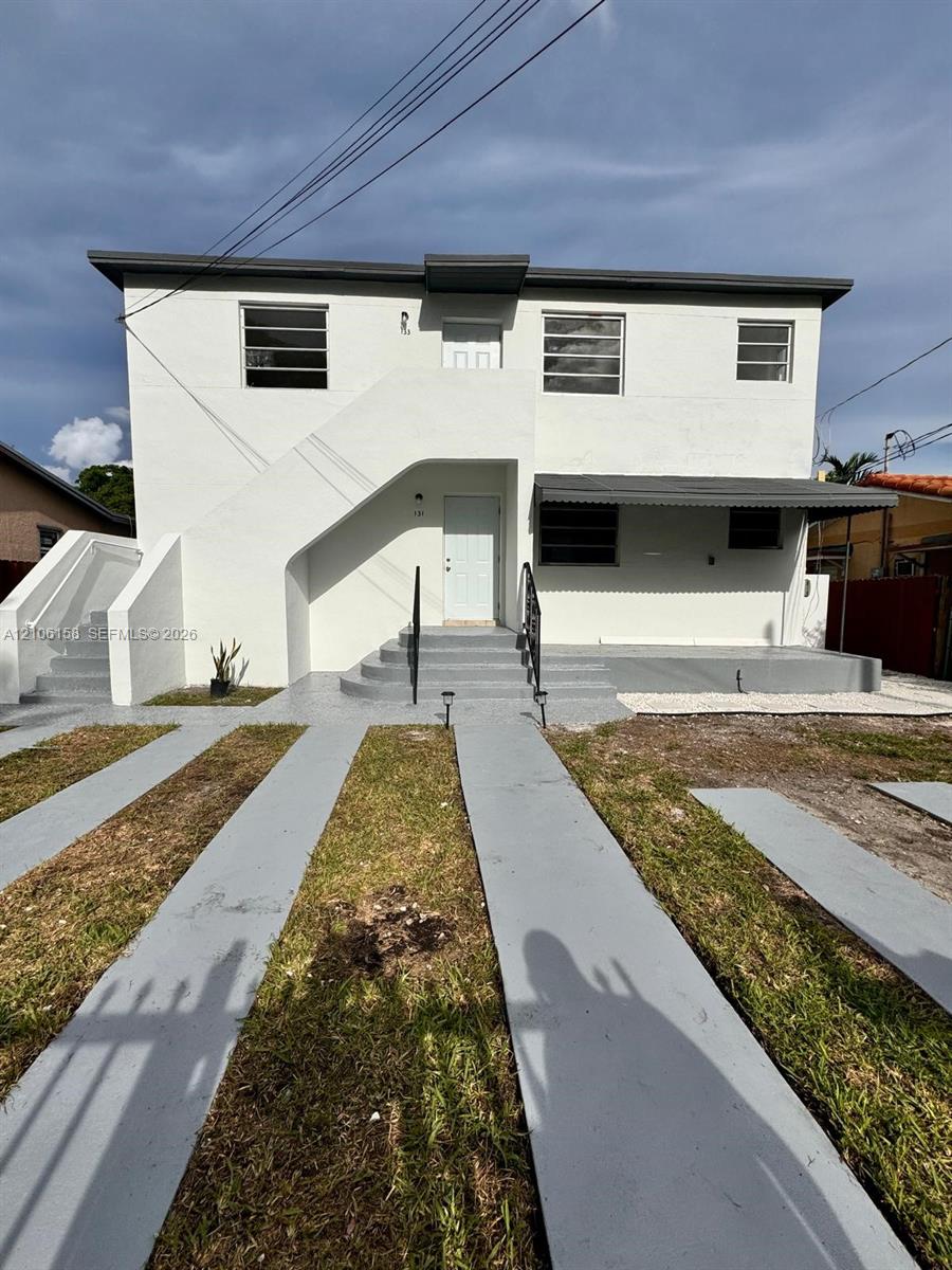 Two-story exterior featuring white stucco finish, multi-pane horizontal windows, metal awning, concrete front steps with metal railing, and concrete driveway strips Two-story exterior featuring white stucco finish, multi-pane horizontal windows, metal awning, concrete front steps with metal railing, and concrete driveway strips
